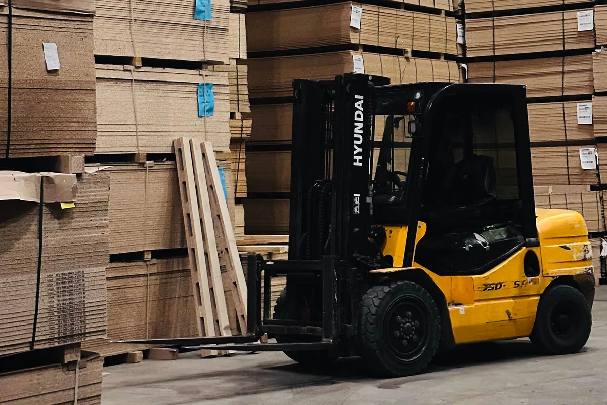 Yellow forklift beside stacked cardboard in an industrial warehouse