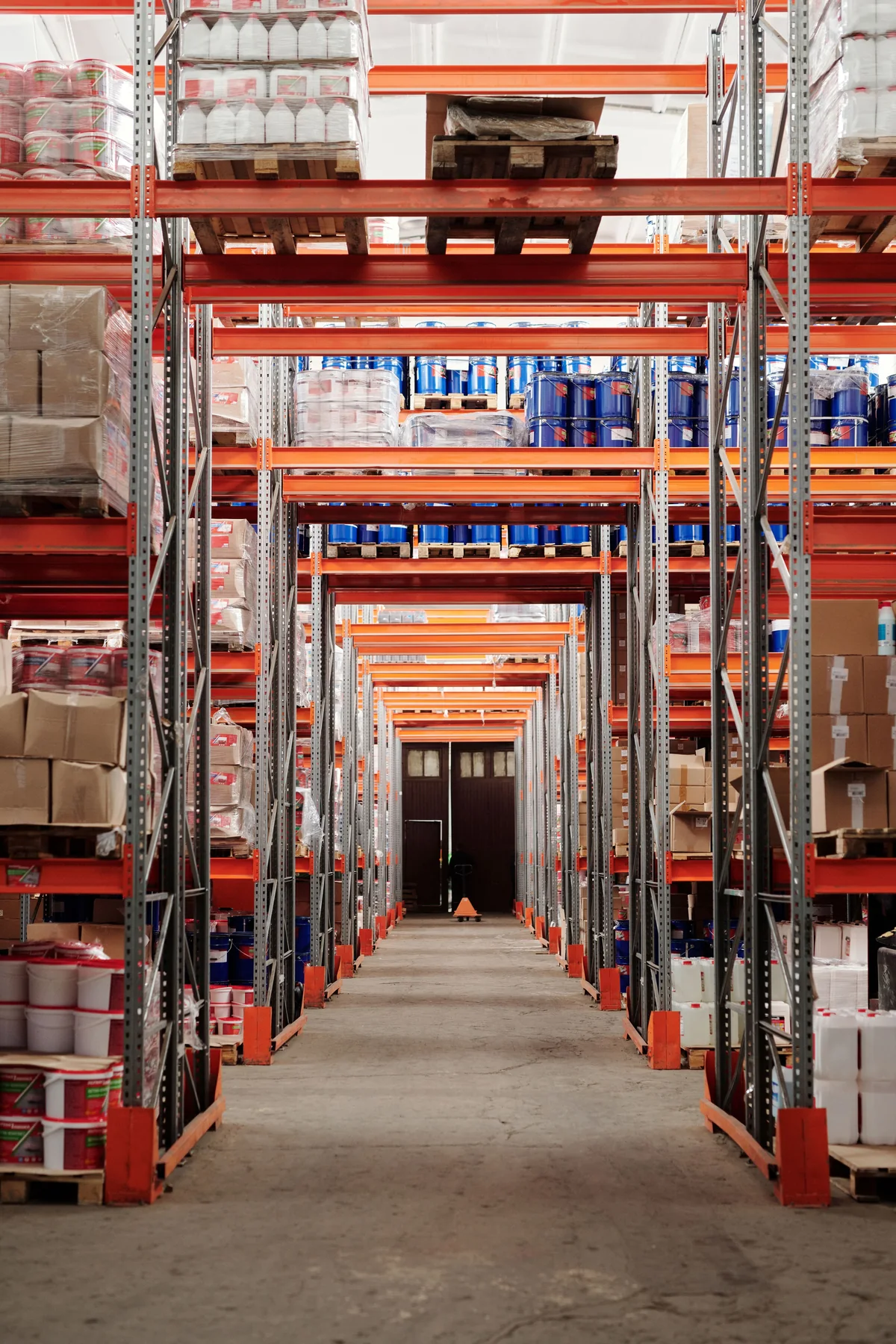 Long aisle between red warehouse racks holding wrapped pallets